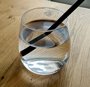 Light rays bend as they travel through the different mediums of air, water, and glass, so the pencil appears deformed.